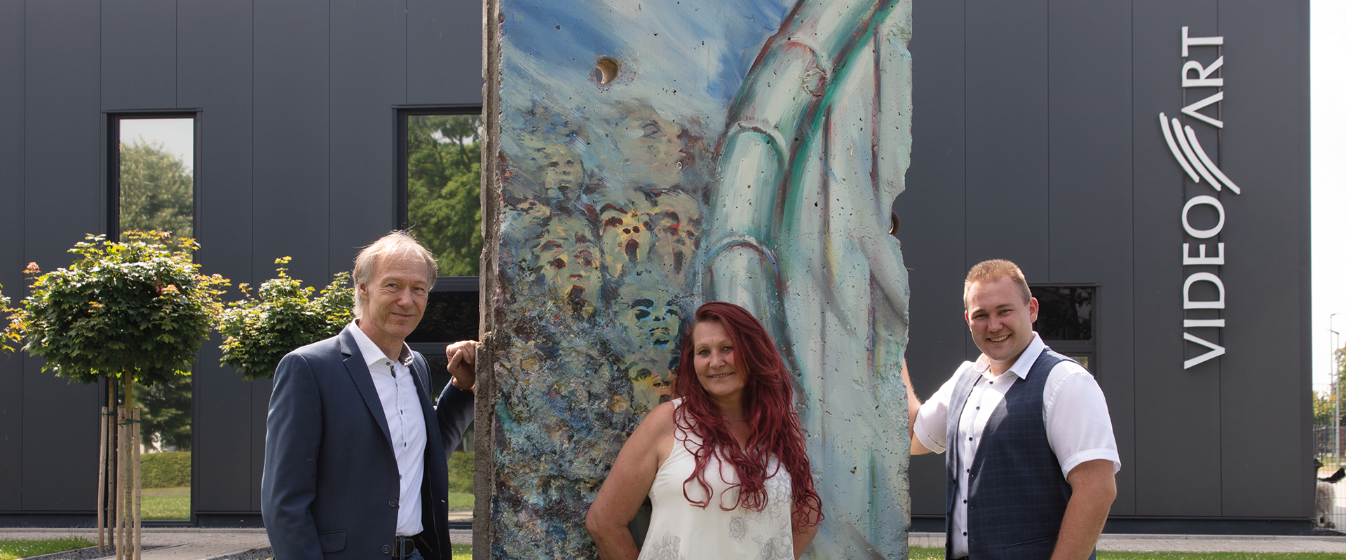 Michael Gillner mit Marion und Sohn vor dem Mauersegment am Firmengebäude der VideoART