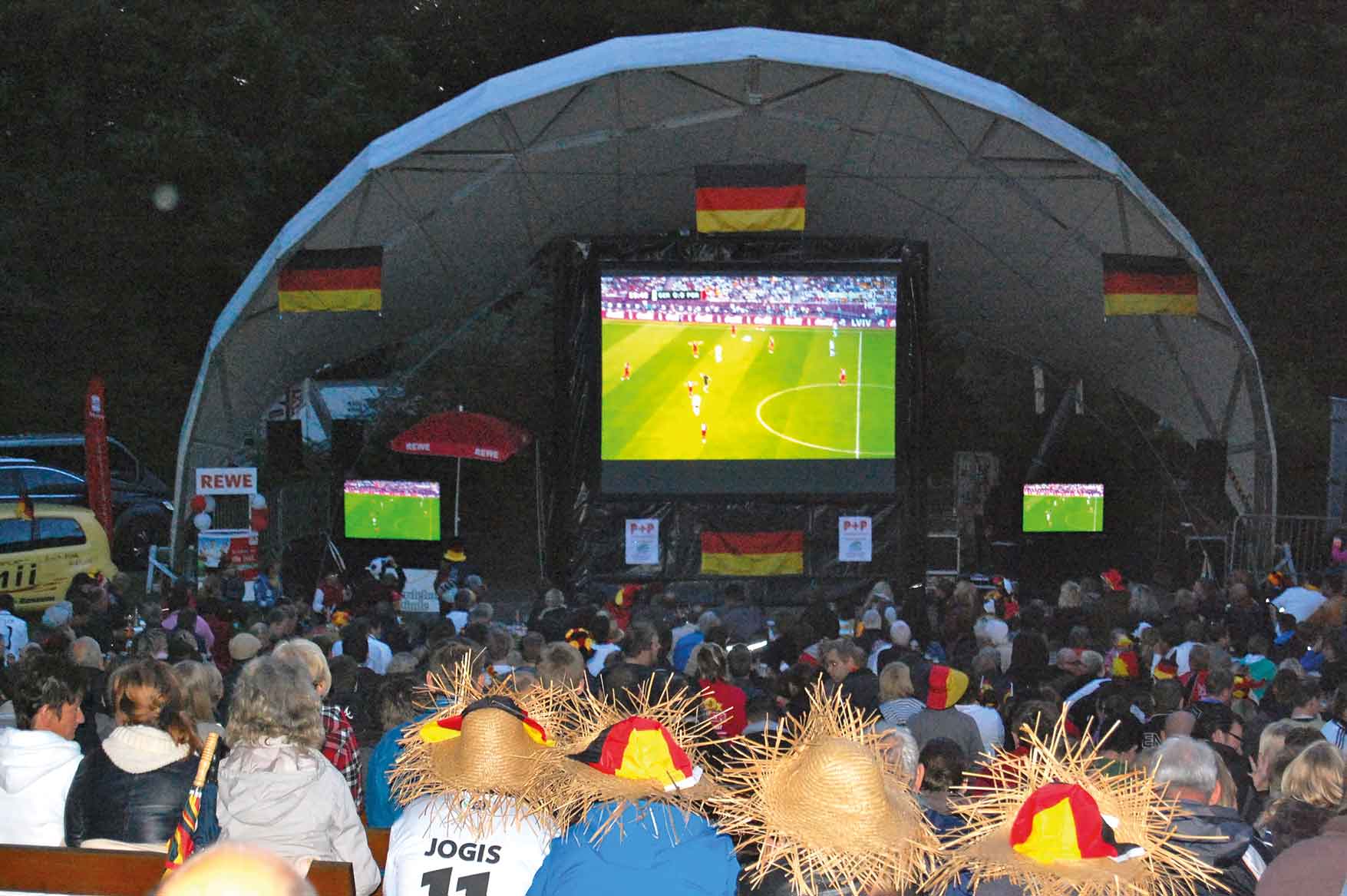 Großbildleinwand mit Fußballspiel und Publikum am Abend im WM-Park
